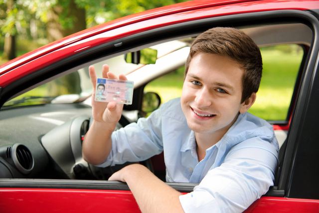 Young driver in a red car holding up a new driver license